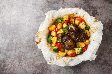 Lamb cooked in its own juices with potatoes, broccoli, onions and peppers in parchment close-up in a frying pan on the table. Horizontal top view from above © FomaA