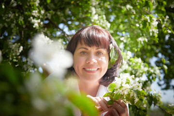 Girl walking and Relaxing near Blossoming apple Tree on Sunny Day. Portrait of Middle aged woman...