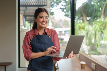 Asian independent business woman wearing overalls while on holiday working outside with laptop...