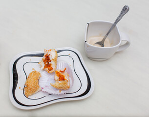 An empty coffee cup and an unfinished dessert plate sit on a white table.
