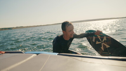 Wakeboarding. A wakeboarder climbs onto a boat after falling into the water. Summer sports on a...