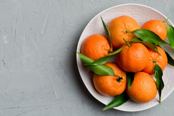 Fresh cutted clementines and whole mandarin over round plate on colored background. Food and drink...