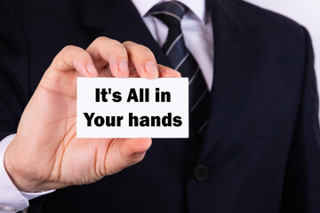 A businessman holding a business card with the words, It's All In Your Hands, written on it.