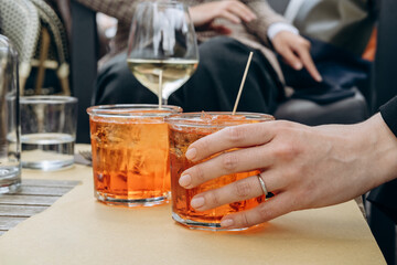 a woman's hand holds a glass of aperol spritz with ice and Prosecco, a traditional Italian aperitif. 