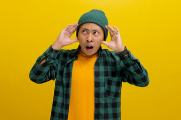 Shocked and anxious young Asian man, dressed in a beanie hat and casual shirt, appears panicked,...