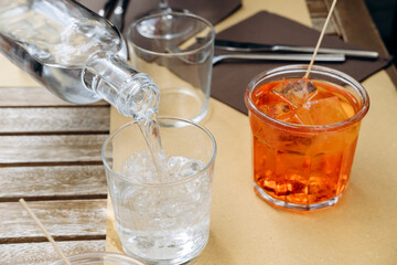 a woman's hand holds a glass of aperol spritz with ice and Prosecco, a traditional Italian aperitif. 