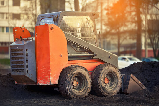 Skid steer loader at construction site. Heavy duty vehicle for earthmoving, grading, and other site preparation tasks. Skid steer loader with bucket attachment, earthmoving work. Mini loader