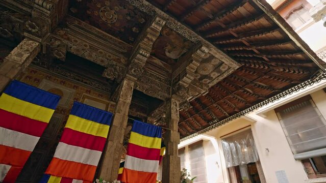 Interior view of Sri Dalada Maligawa with ornate wood carvings, colorful Buddhist flags in Kandy. Sacred temple architecture, pilgrims visit, worship ancient relic site in Sri Lanka.