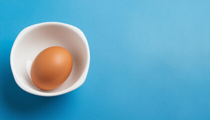Single egg in the white bowl with blue background, copyspace on a side