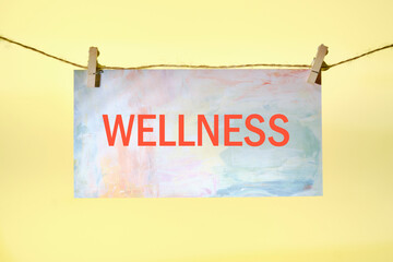 Wellness sign written on paper suspended from a rope on a yellow background