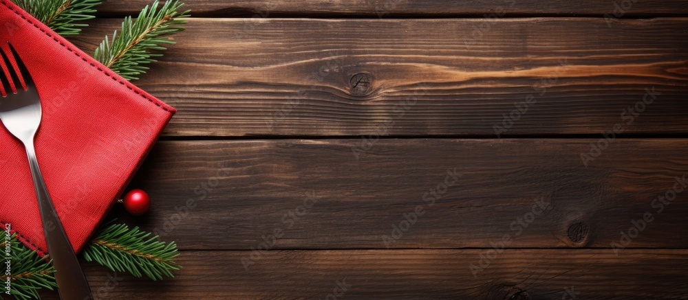 Poster Top view of a red napkin with a wooden background showcasing a spoon knife and fork alongside a fir tree branch Ample copy space available for showcasing your content such as a menu or advertising