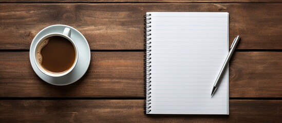 A copy space image featuring a close up view of a coffee cup pen and notebook placed on a wooden background