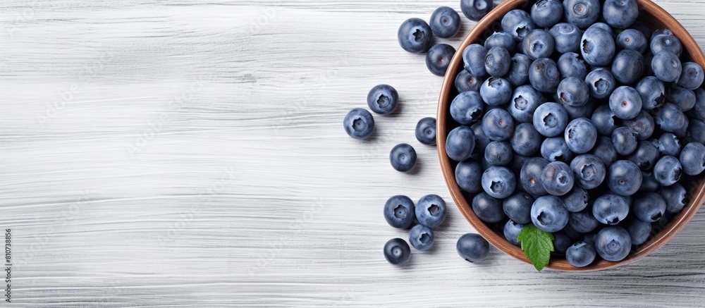 Poster a summery image of ripe blueberries arranged in a blue bowl on a white wooden surface seen from abov