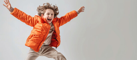 A happy little girl with curly hair is jumping and laughing, wearing an orange jacket over a white t-shirt and beige pants on the right side