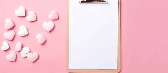 Top view of a clipboard with a white paper on a pink background The composition features hearts making it perfect for Valentine s Day Mother s Day or a wedding theme There is a generous copy space av