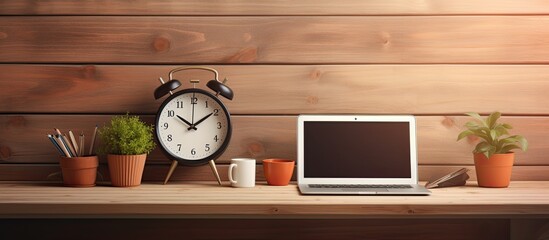 A copy space image of a beautifully arranged workstation for a creative designer containing a blank laptop a plant a decorative bowl a clock and pencils all placed on a wooden plank background