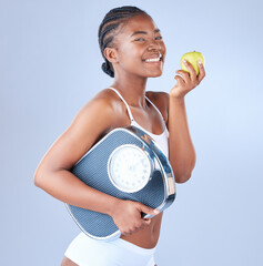 Happy black woman, portrait and scale with apple for diet, nutrition or vitamins on a blue studio...