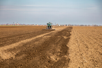 Tractor preparing soil in an expansive agricultural field with village backdrop
