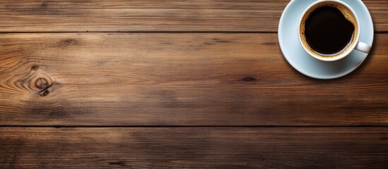 Top view of a cup of coffee resting on a wooden table with ample space in the image for copying and pasting