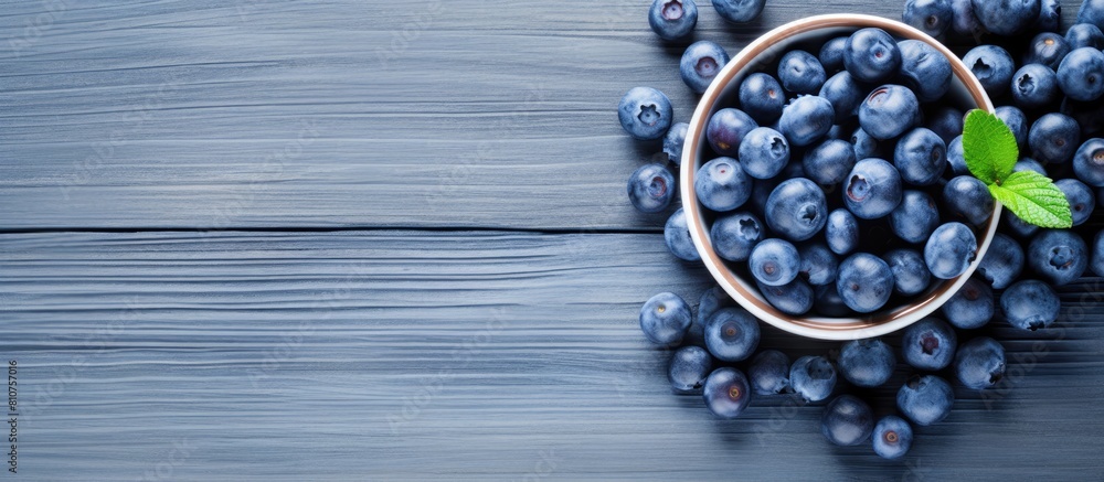 Poster a summery image of ripe blueberries arranged in a blue bowl on a white wooden surface seen from abov
