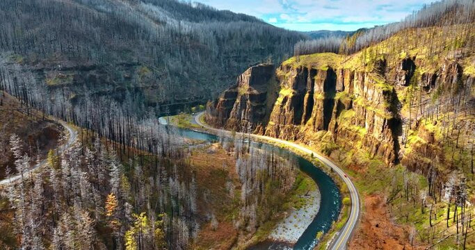Empty highway at the foot of the mountain along the narrow river. One car riding by the road among the rocks. Oregon wilderness. Aerial view.