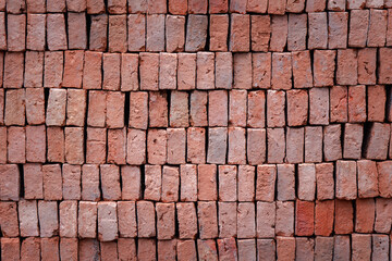 This is a close-up photo of a large pile of red bricks. The bricks are stacked in layers, appearing quite unevenly arranged, allowing the texture and small cracks of each brick to be seen.
