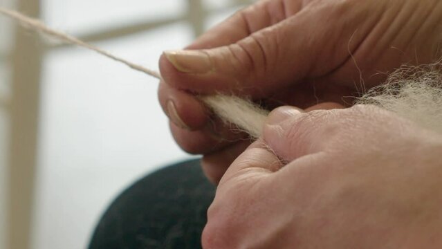 Closeup hands pull natural wool into spinning wheel, making grey yarn