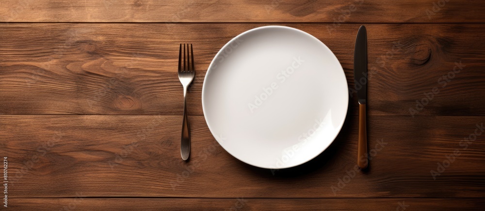 Poster a concept image of white plate fork and knife placed on a wooden table along with cutlery and silver