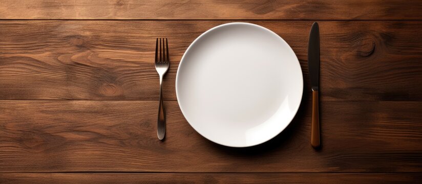 A concept image of white plate fork and knife placed on a wooden table along with cutlery and silverware. Creative banner. Copyspace image