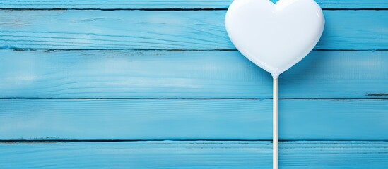 Close up of a Valentine s Day heart shaped lollipop and a white frame on a blue wooden background with copy space image