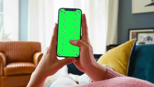 Close up POV shot of woman lying on sofa at home scrolling through social media,messages or online on green screen mobile phone - shot in slow motion