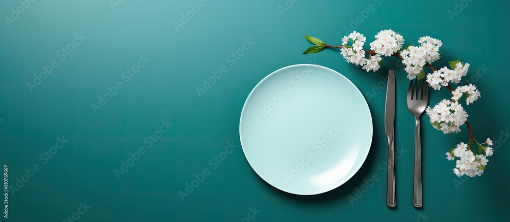 Poster A turquoise table serves as the backdrop for an empty white dish accompanied by a knife and fork A cotton branch adds a touch of elegance Copy space image available for menu or recipe