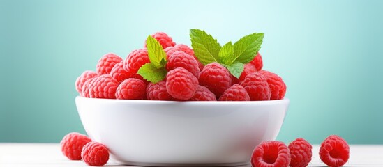 A closeup copy space image of a bowl containing fresh raspberries and mint leaves placed on a light...