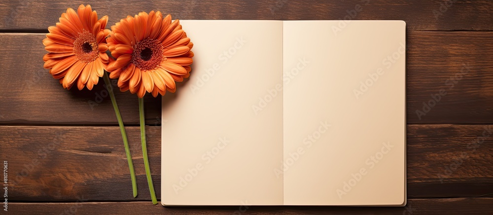 Poster Top view copy space image of three gerbera flowers and a blank paged notebook resting on a wooden table
