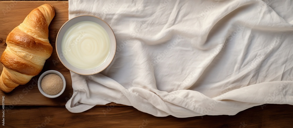 Poster On a wooden table there is a top view of a fresh croissant placed on white fabric Additionally there is an egg in a paper panel and a rolling pin with flour in a bowl nearby creating a lovely copy sp