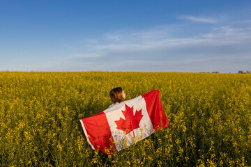 woman stands with her back among a yellow, flowering rapeseed field and proudly holds a large...