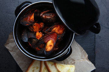 A dish of mussels. Fresh mussels in a black saucepan in tomato sauce. A traditional seafood dish. White bread crackers. Top view. Copy space.