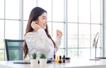 Asian beautiful smiling happy female sitting at home and doing her make-up near mirror morning....