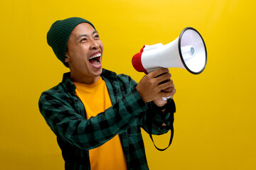 Excited Asian man in a beanie hat and casual shirt makes an announcement with a megaphone, using a...