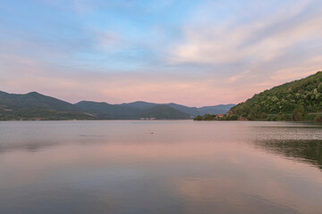  A serene sunset over a tranquil lake with rippled water, mountains in the distance, and a clear sky with soft clouds