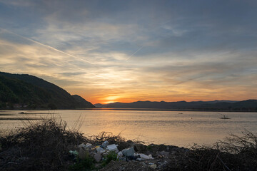  lake scene at sunset is marred by the presence of pollution and garbage along the shore, highlighting the pressing issue of environmental degradation and the need for pollution awareness...