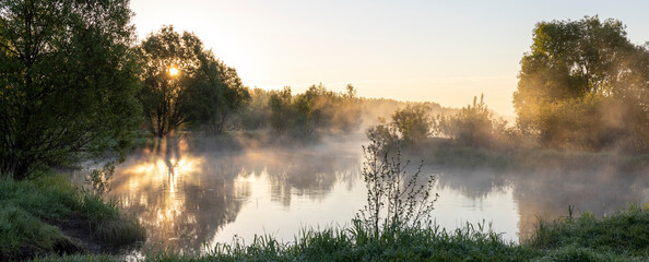 dawn by the river, sun rays through the fog, early morning