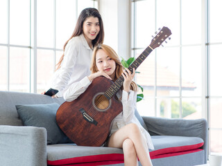 Two asian couple beautiful woman playing acoustic guitar, sing folk song together sitting on sofa...