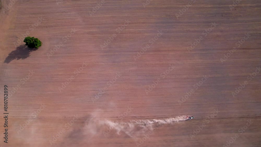 Poster aerial top down tracking follows tiny tractor ploughing with dust cloud trailing behind