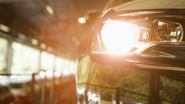 Car headlight turning on in a dimly lit garage with a sunlit background, featuring a panning shot