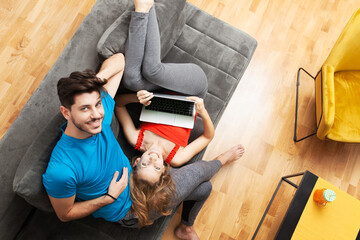 Cheerful young man and woman enjoying a relaxed day at home with the woman lying upside down using...
