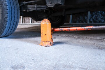 The orange hydraulic bottle jack is installed under car, stock photo.