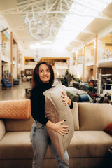 Portrait of young woman choosing pillow at store of household goods