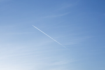 Tiny flying plane in blue sky with trail