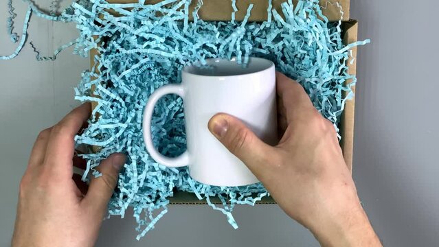 pack in a cardboard box. paper filler. white mug. mug as a close-up. Slow-motion video. High quality video in 4K format.
